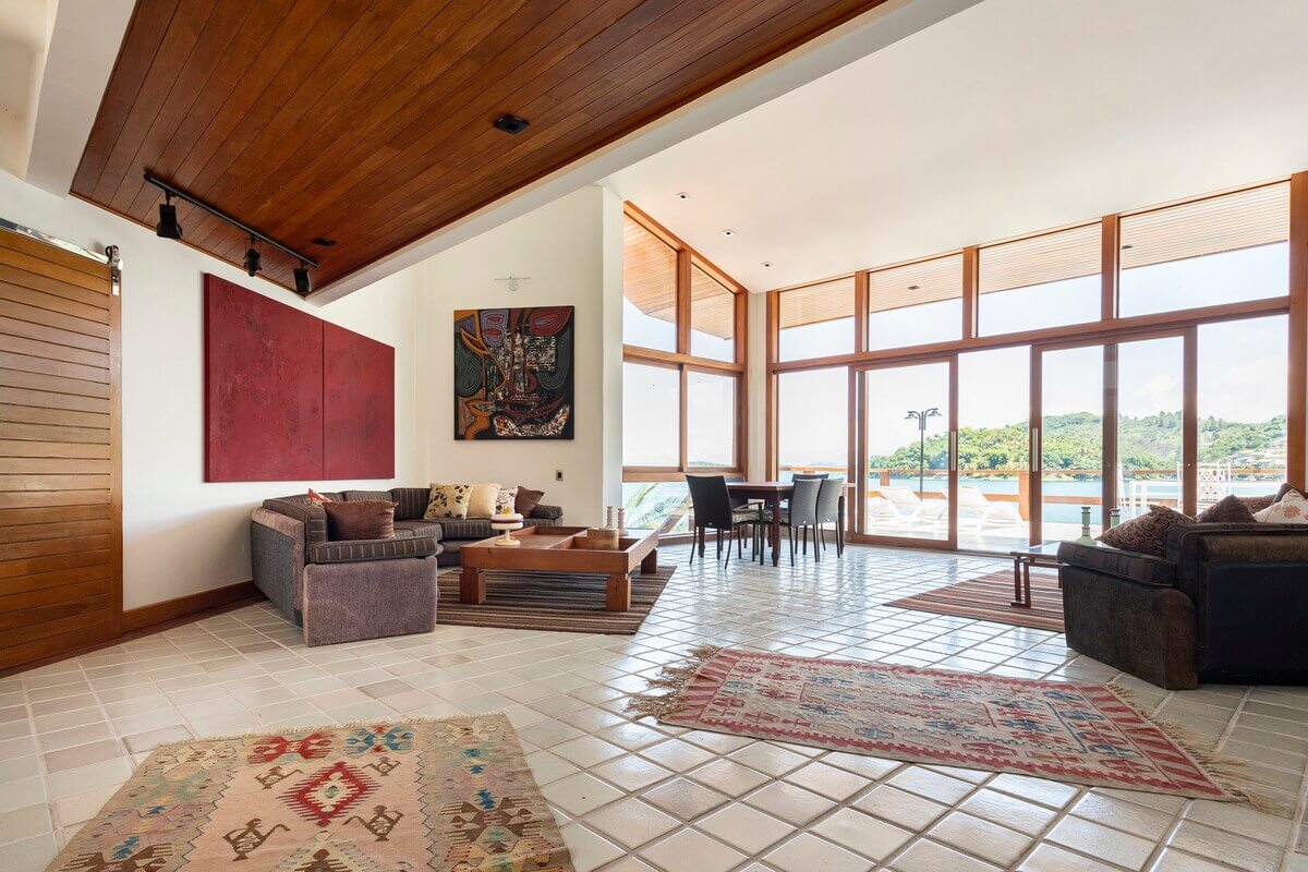 Espaçosa suíte climatizada da Casa Kaîre, com design contemporâneo e amplas janelas oferecendo vista direta para a Baía da Ribeira.